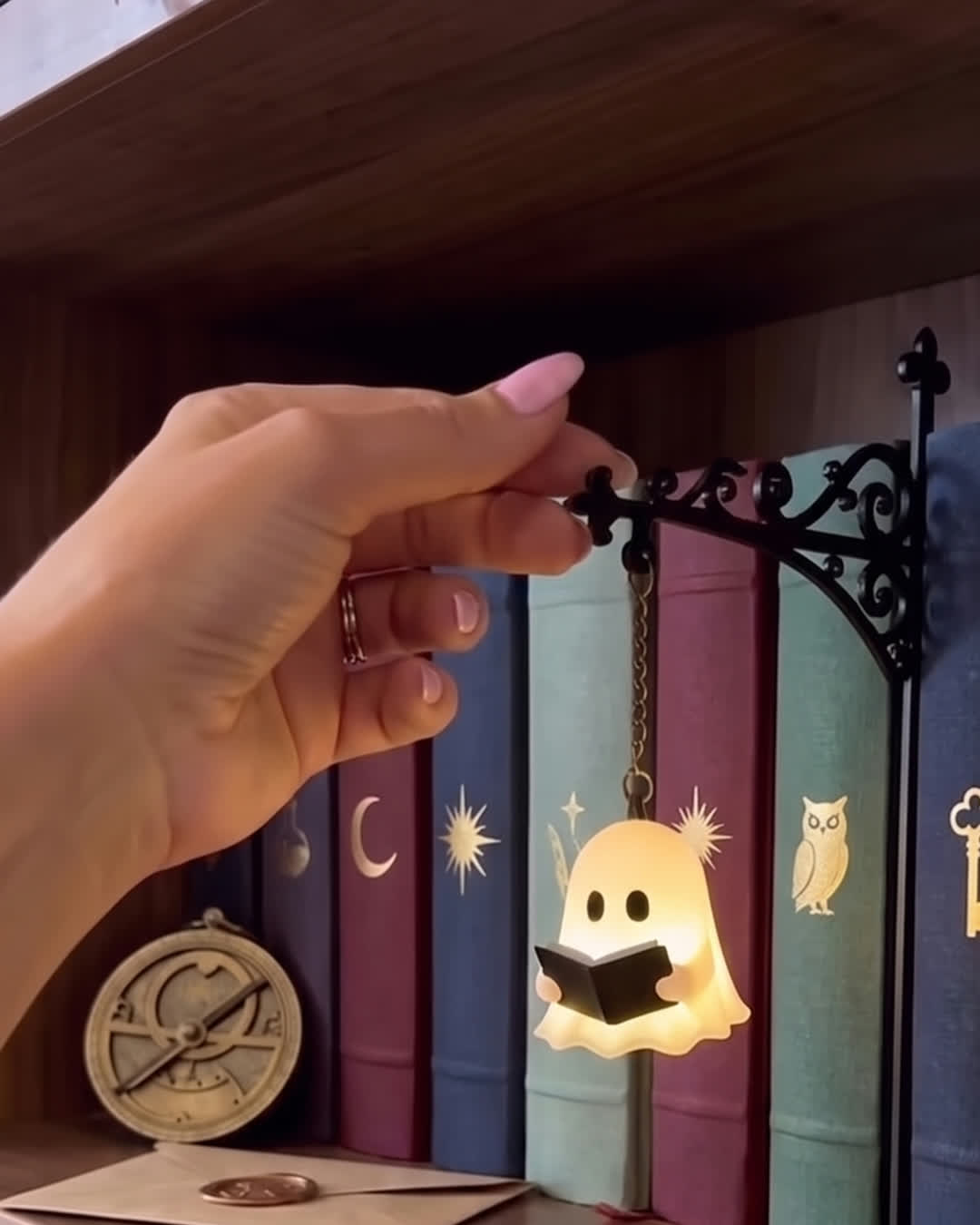 Ghost Reading bookshelf lamp glowing on a walnut shelf of jewel-toned books
