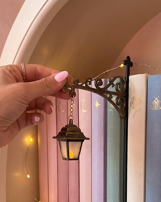 Vintage Lantern bookshelf lamp glowing between pastel clothbound books
